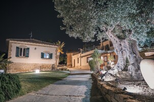 Un edificio de piedra con techo de tejas, un camino empedrado y un gran árbol de follaje denso.