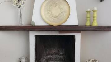 Una chimenea con repisa blanca, un plato decorativo y dos candelabros amarillos.