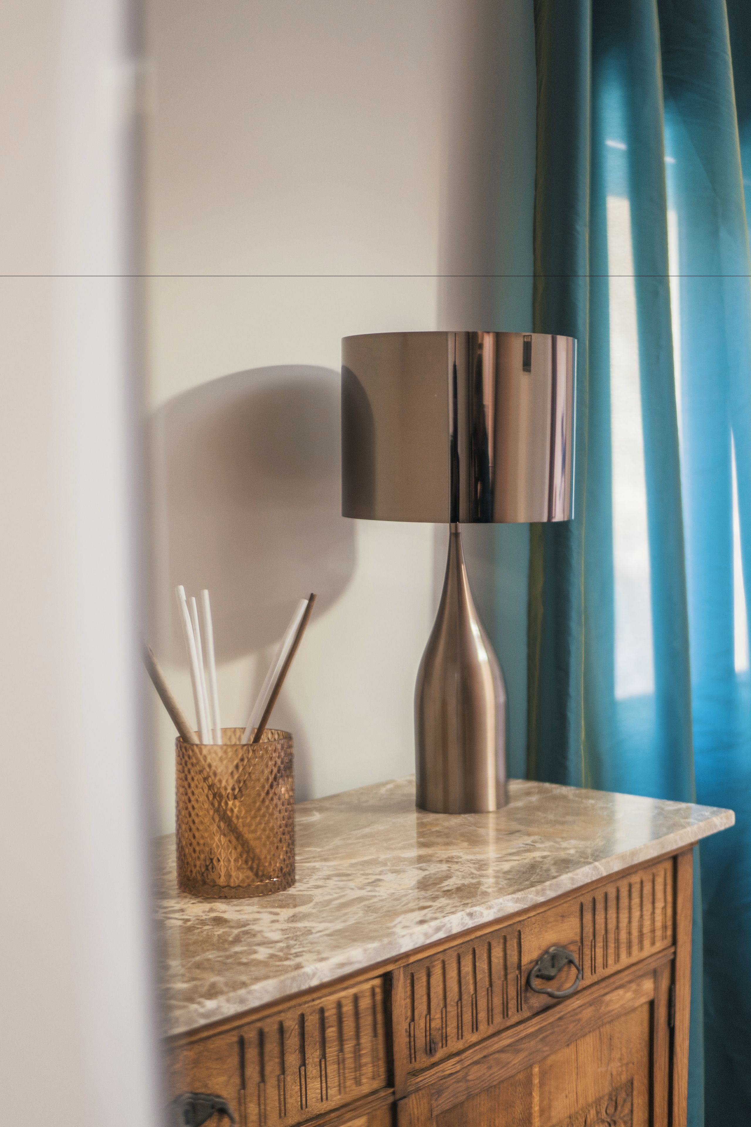 A wooden cabinet with a marble countertop, a metal lamp, and a woven container holding straws.