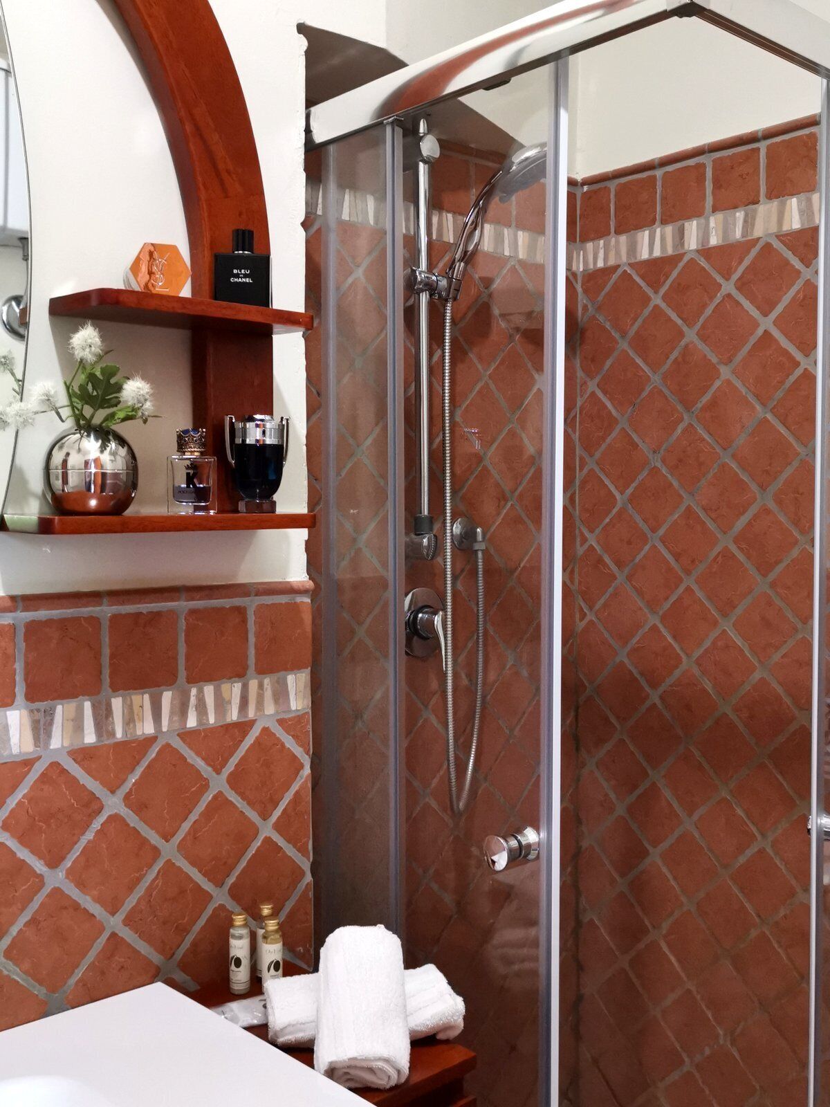 Un baño con ducha, tocador con espejo y repisa con artículos de aseo.