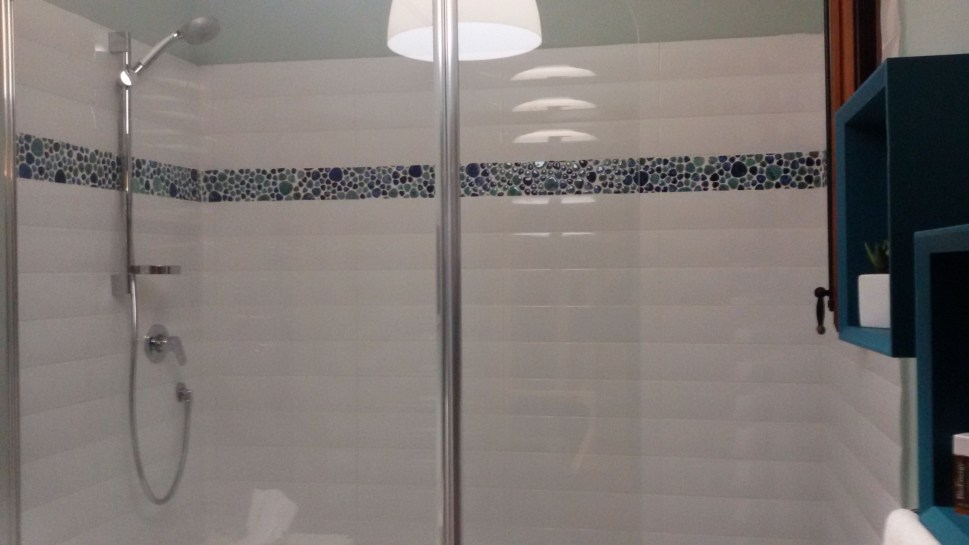 A glass-enclosed shower with a handheld showerhead and a wall-mounted faucet.