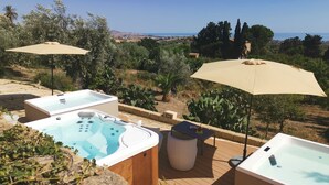 Zona de hidromasaje con dos sombrillas beige, una terraza de madera y vistas al mar y al paisaje.
