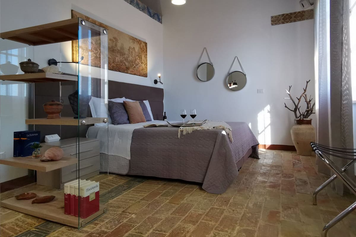 Een slaapkamer met een bed, planken, een spiegel en een vaas.