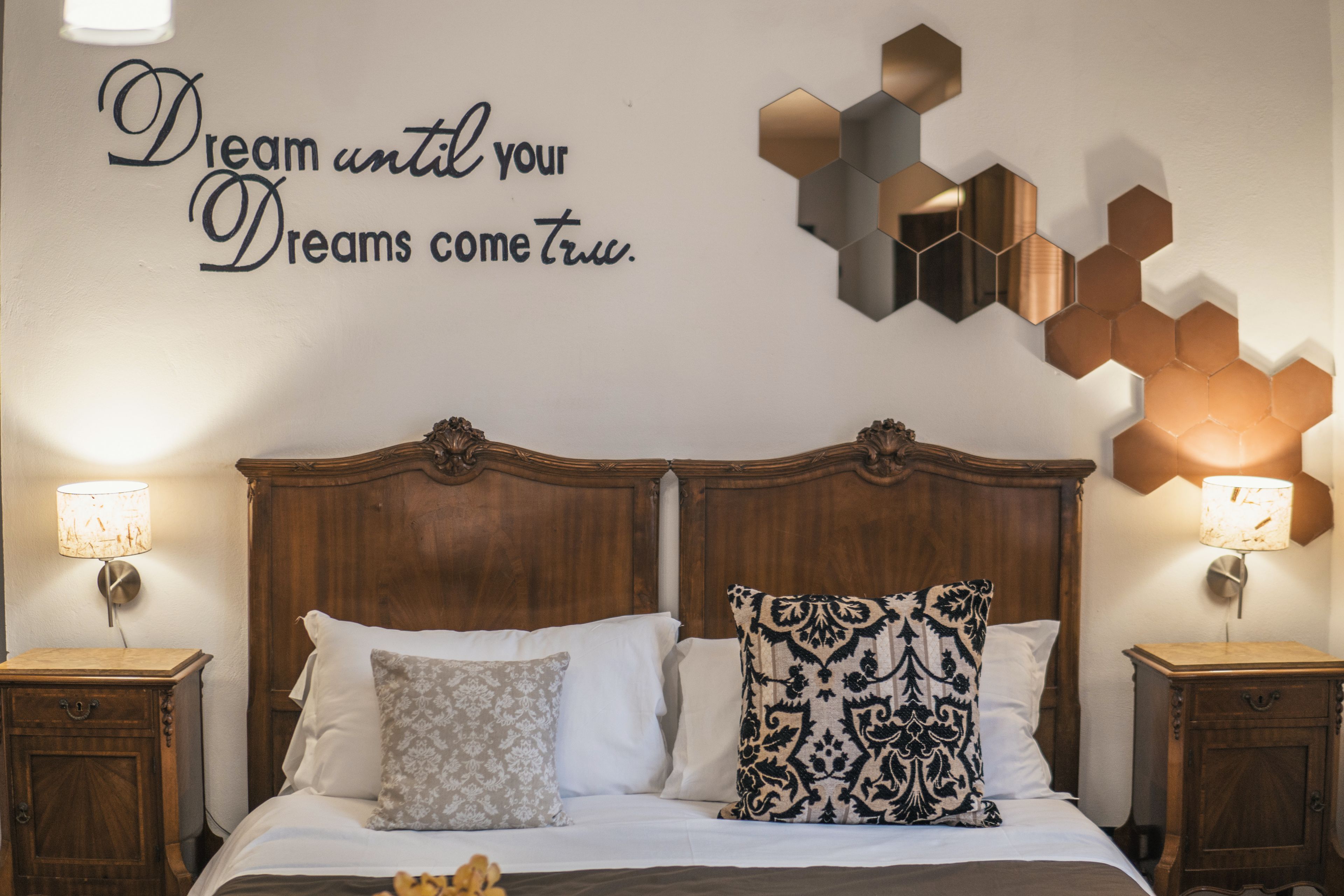 A neatly made bed with a decorative wall above it, a wooden headboard, and two bedside tables with lamps.