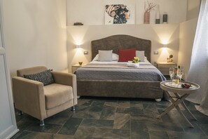 Ein Schlafzimmer mit einem großen Bett, einem Sessel, einem kleinen Tisch mit Tablett und einem an der Wand hängenden Kunstwerk.