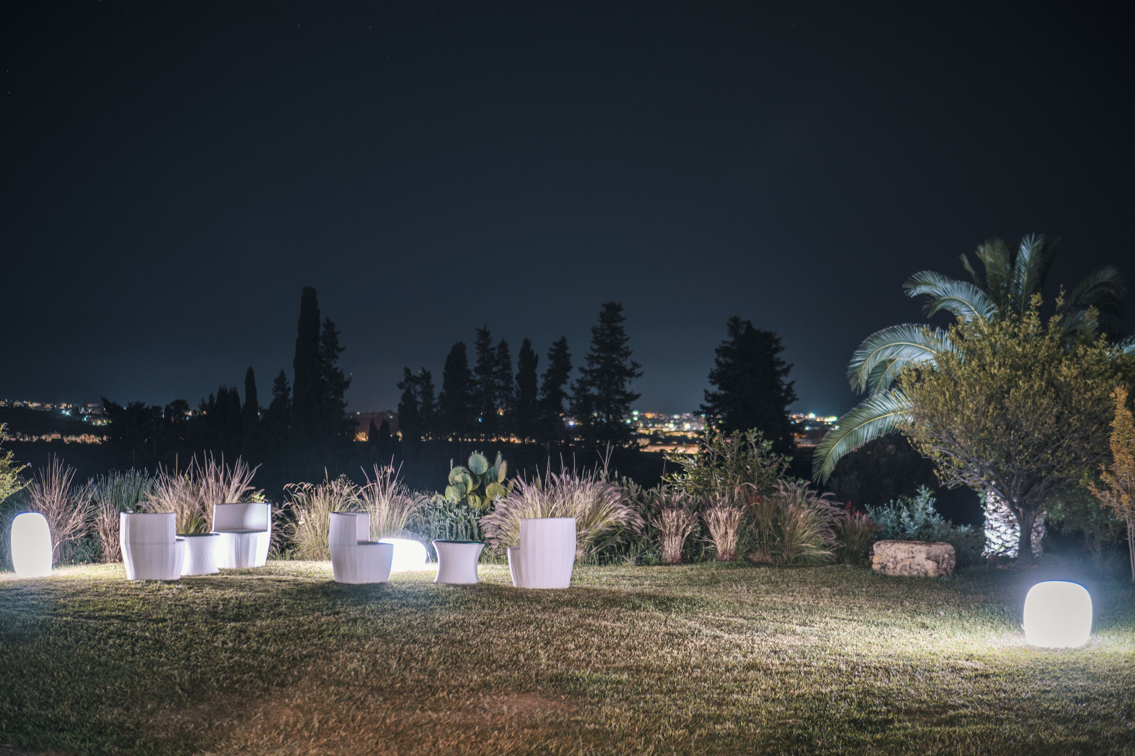 Un espacio exterior nocturno con plantas en macetas y un objeto grande iluminado.
