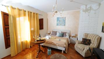 A bedroom with a bed, bedside table, chair, and a chandelier.