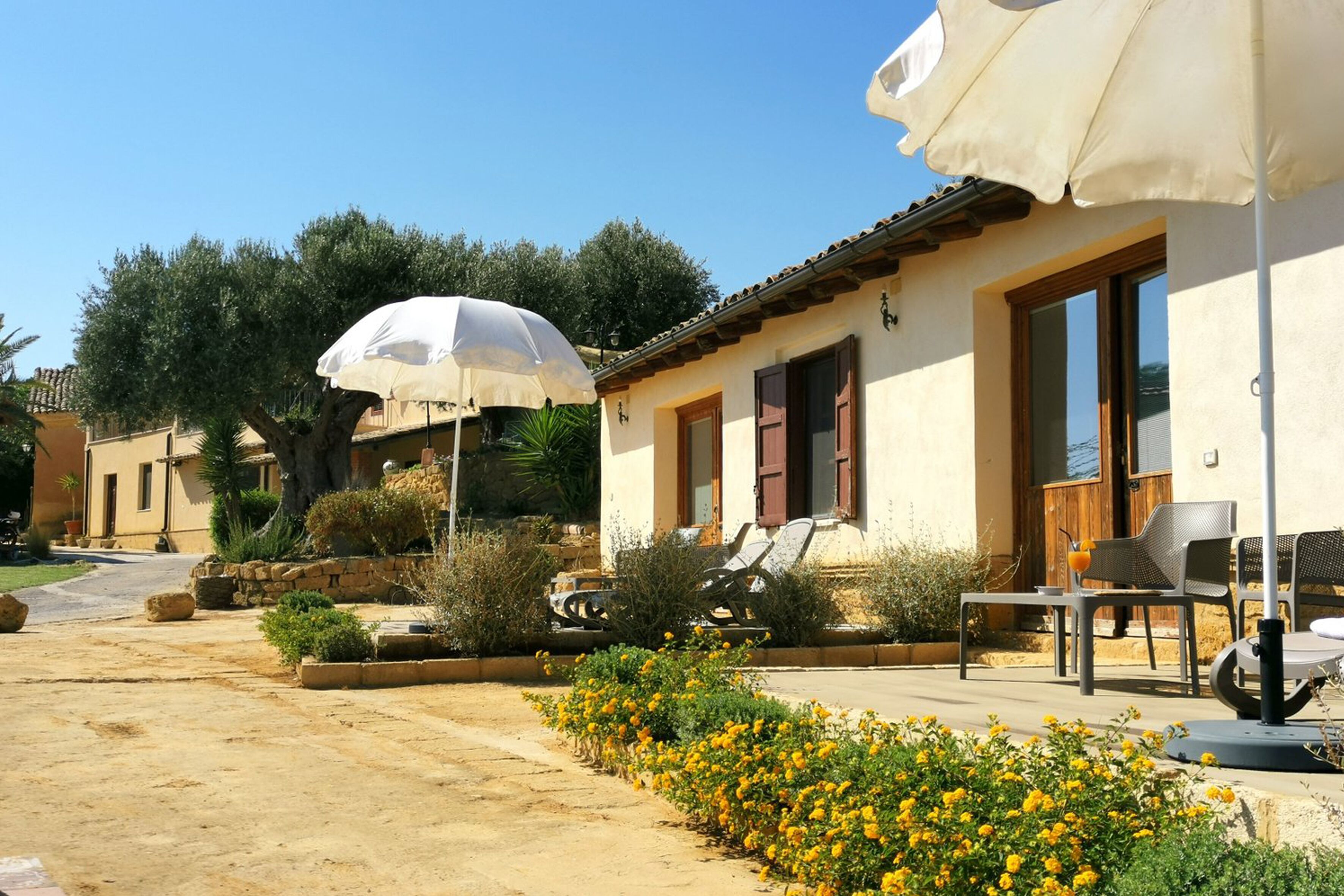 A sunny outdoor seating area with a table and chairs, a white umbrella, and a stone pathway.
