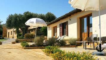 A sunny outdoor seating area with a table and chairs, a white umbrella, and a stone pathway.