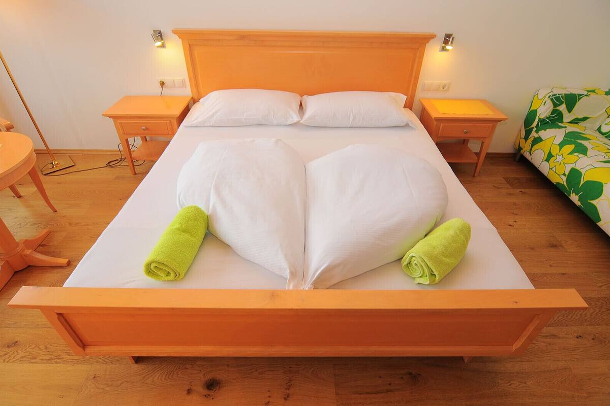 A bed with a heart-shaped pillow arrangement and two rolled towels.