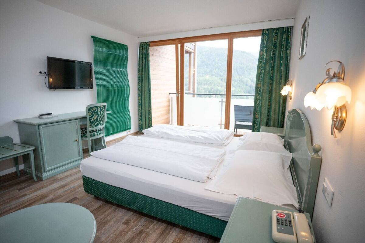 A hotel room with a bed, a desk, a chair, a telephone, and a television.