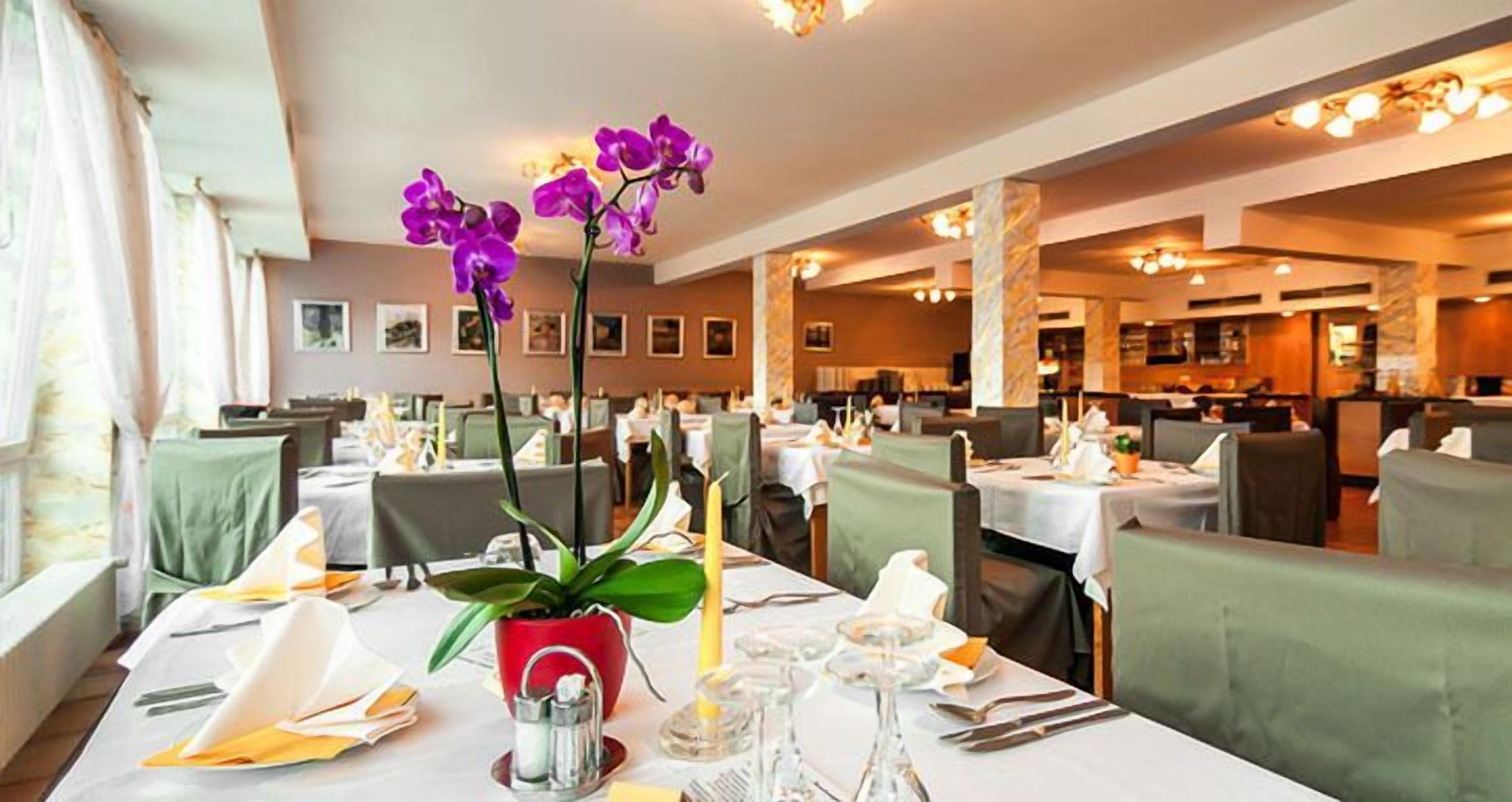 A restaurant with tables set for dining, featuring a vase with purple orchids and a red pot with green leaves.