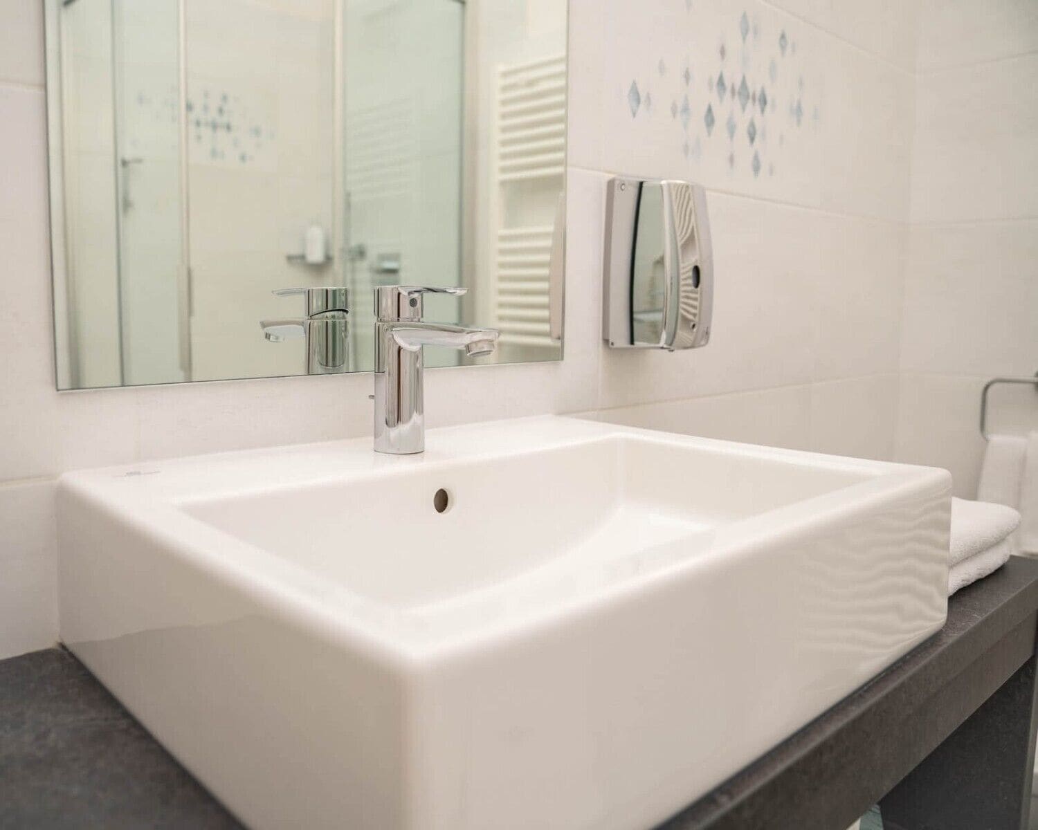 Een moderne badkamer met een witte wastafel, een chromen kraan en een spiegel.