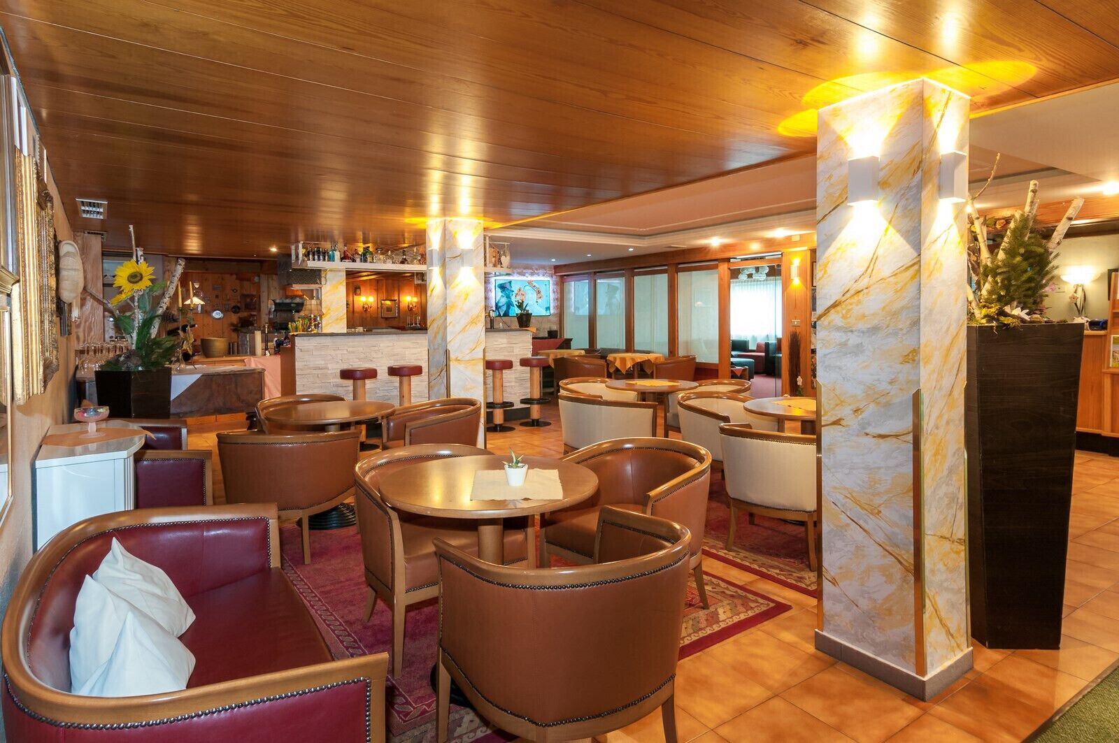 A restaurant with wooden furniture, marble pillars, and a bar area.
