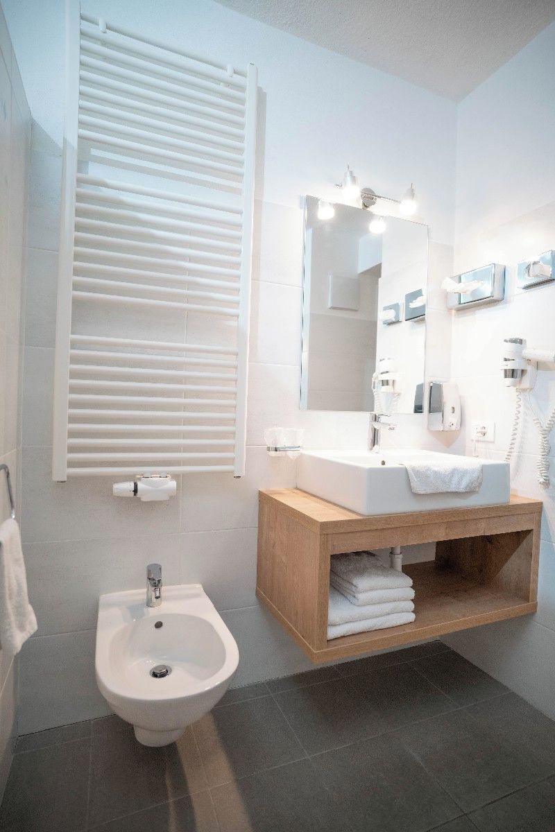 Un baño moderno con un bidé, un lavabo con espejo y un perchero para toallas.