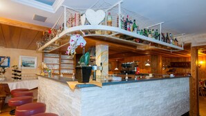 A bar area with a white brick counter, red bar stools, and a variety of bottles and glasses on shelves above. - Hotel Panoramik (Rio di Pusteria)