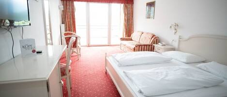 A hotel room with a bed, a desk, a chair, a sofa, and a television.