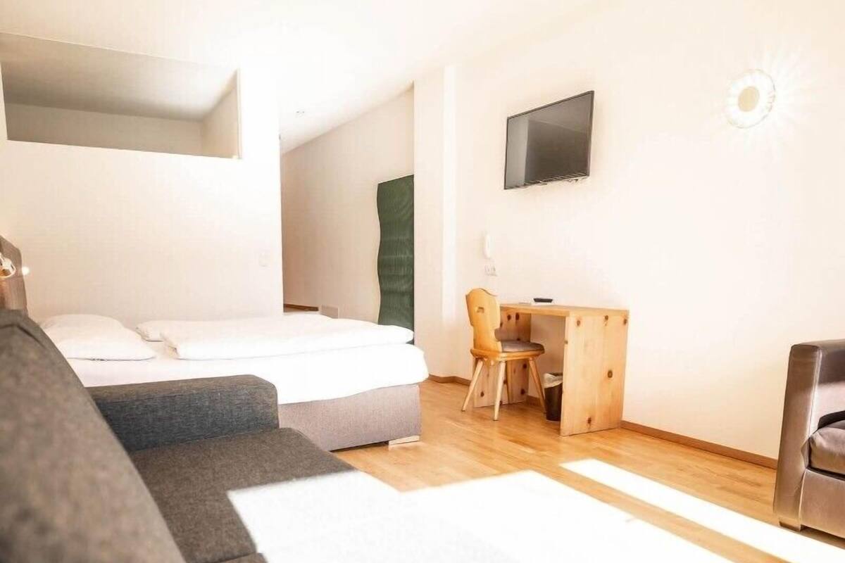 A modern hotel room with a sofa, a bed, a desk, and a TV.