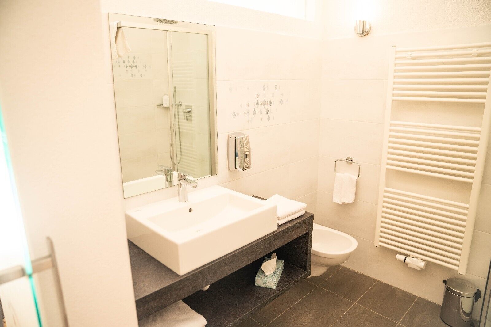 A modern bathroom with a white sink, mirror, and toilet.