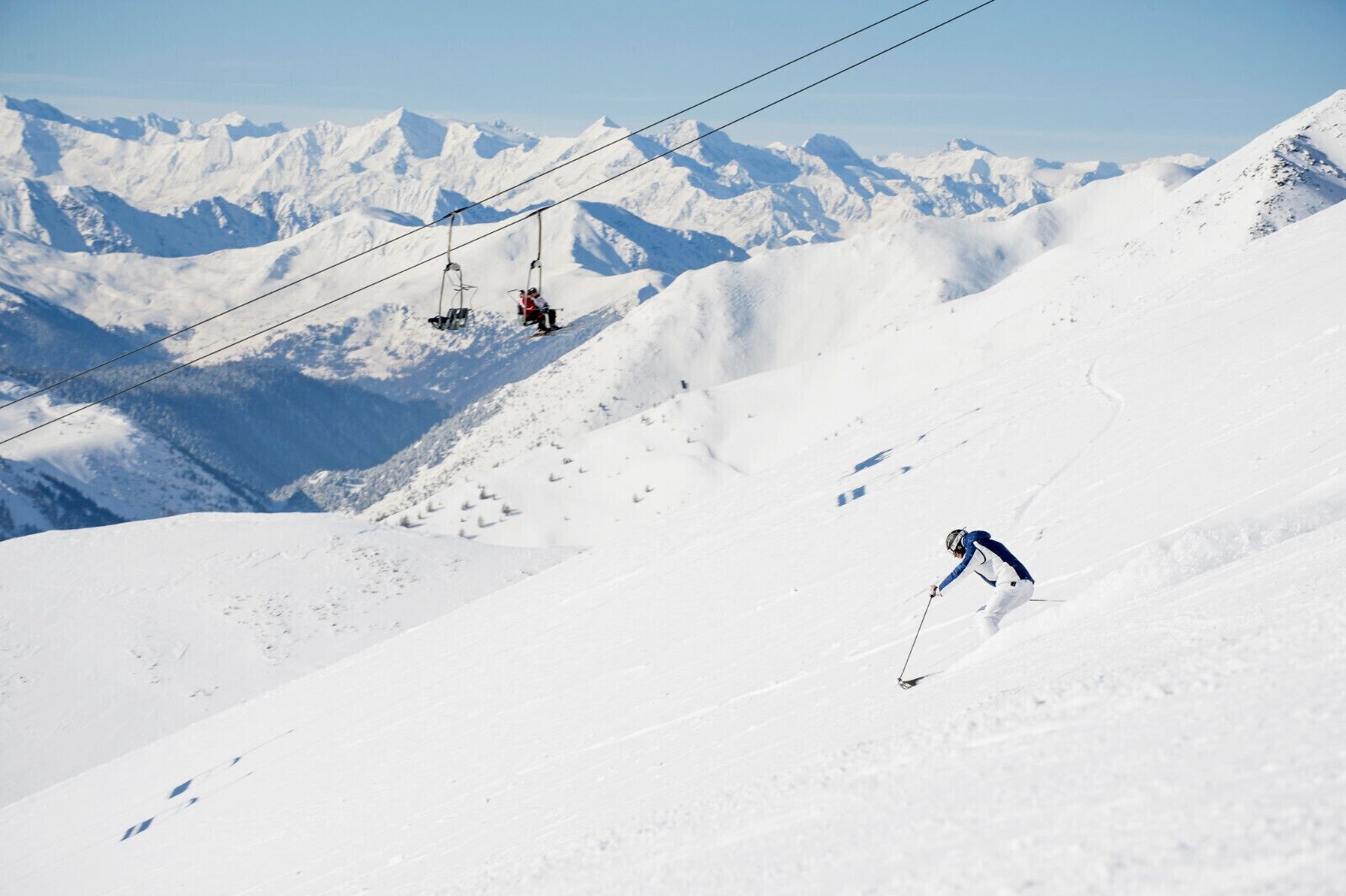 Een besneeuwde helling met een skilift en een skiënde persoon die naar beneden gaat.