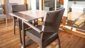 A wooden deck with a table and wicker chairs, large glass doors leading to a balcony with a view of the sea. - Hotel Panoramik (Rio di Pusteria)