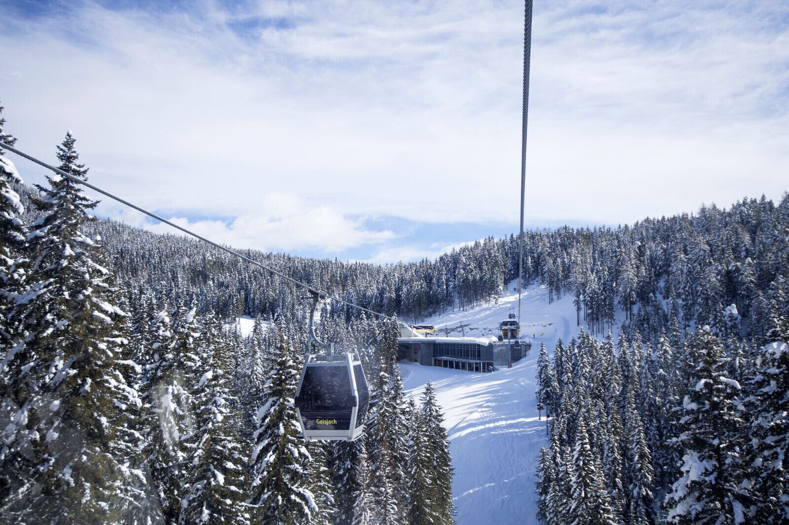 A cable car moving through a snowy forest with a clear sky.