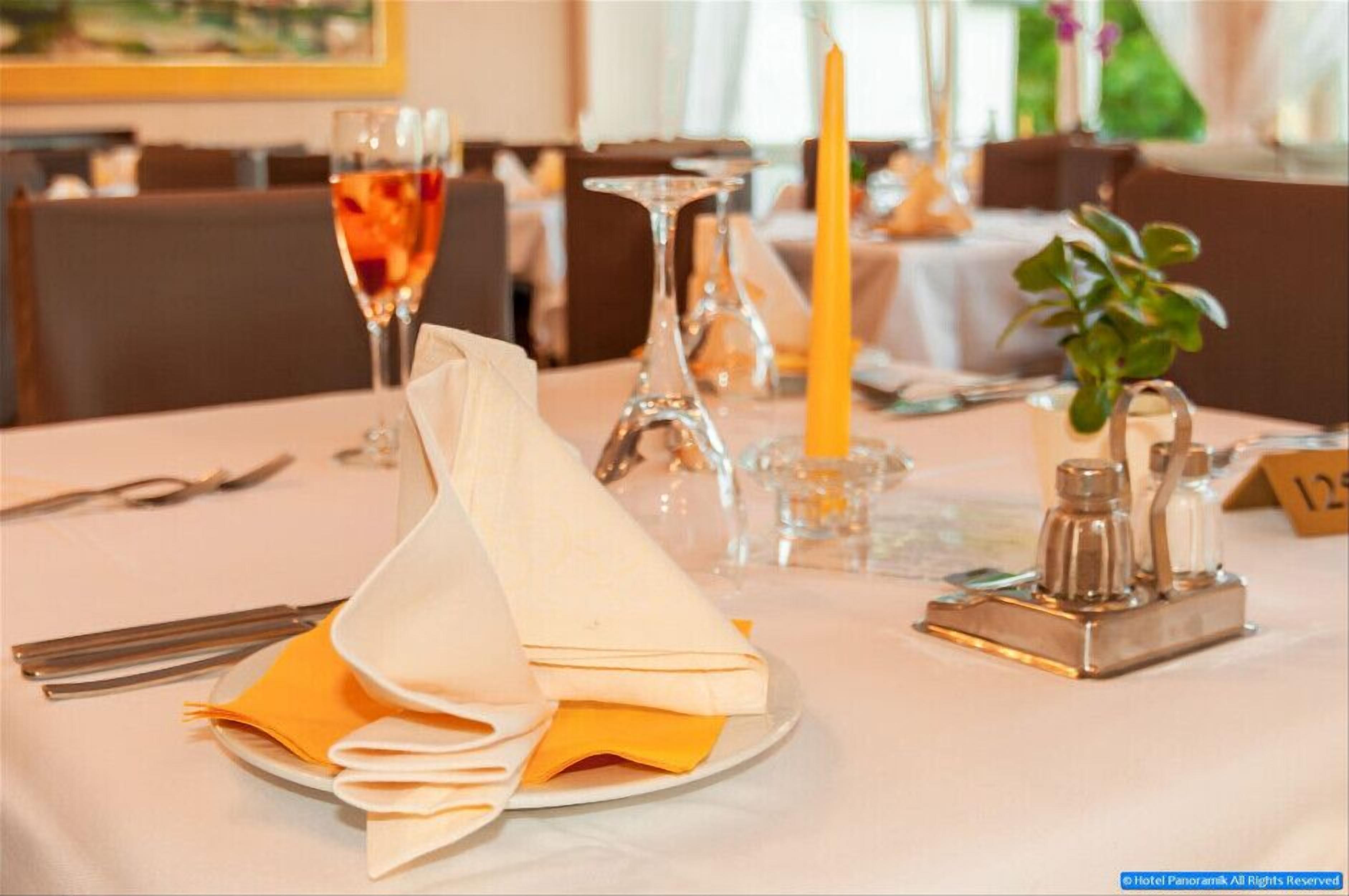 A dining table set with a folded napkin, a glass of red wine, a candle, salt and pepper shakers, and a small plant.