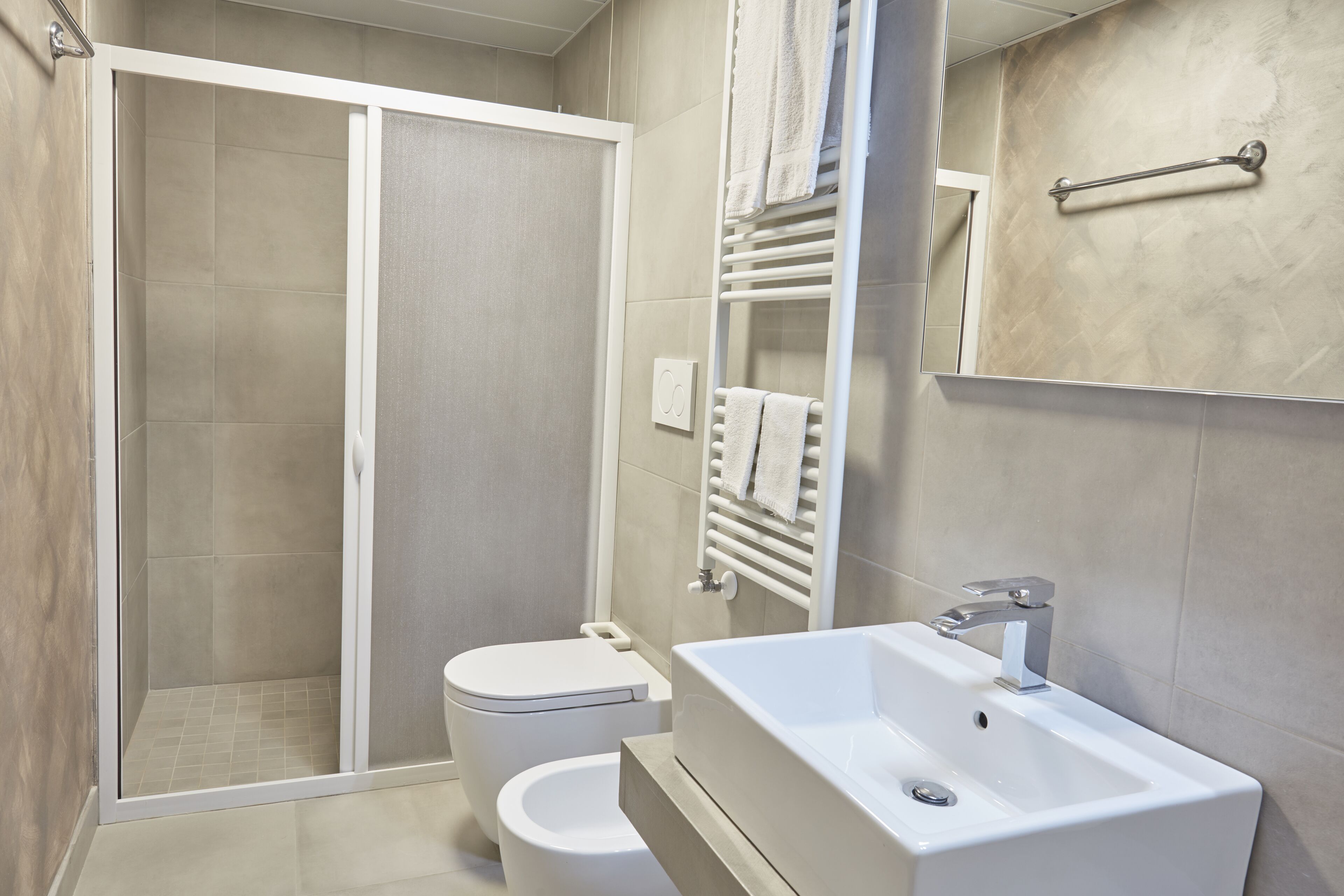 Une salle de bain moderne avec une douche, des toilettes et un lavabo surmonté d’un miroir.
