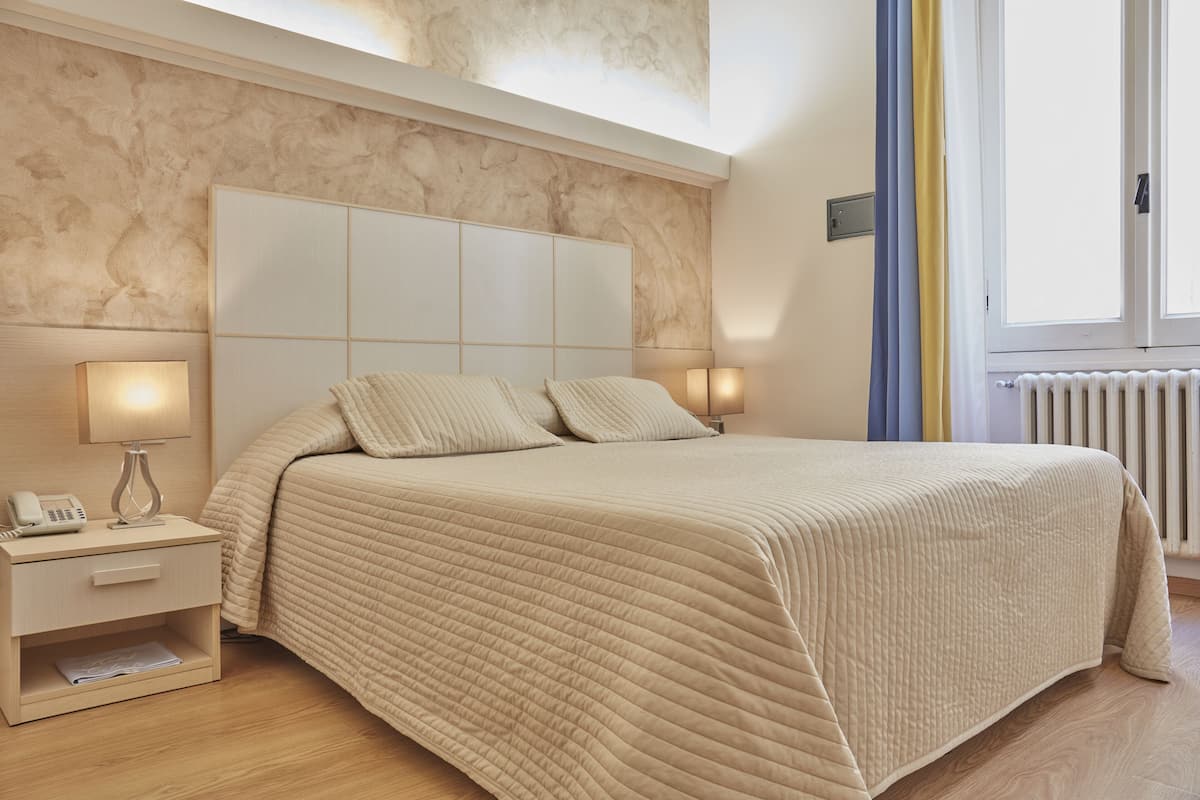 Une chambre à coucher avec un grand lit, des lampes de chevet, une table de nuit et une fenêtre avec des rideaux.
