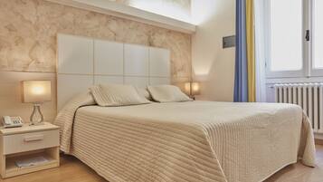 A bedroom with a large bed, bedside lamps, a nightstand, and a window with curtains.