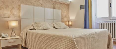 A bedroom with a large bed, bedside lamps, a nightstand, and a window with curtains.