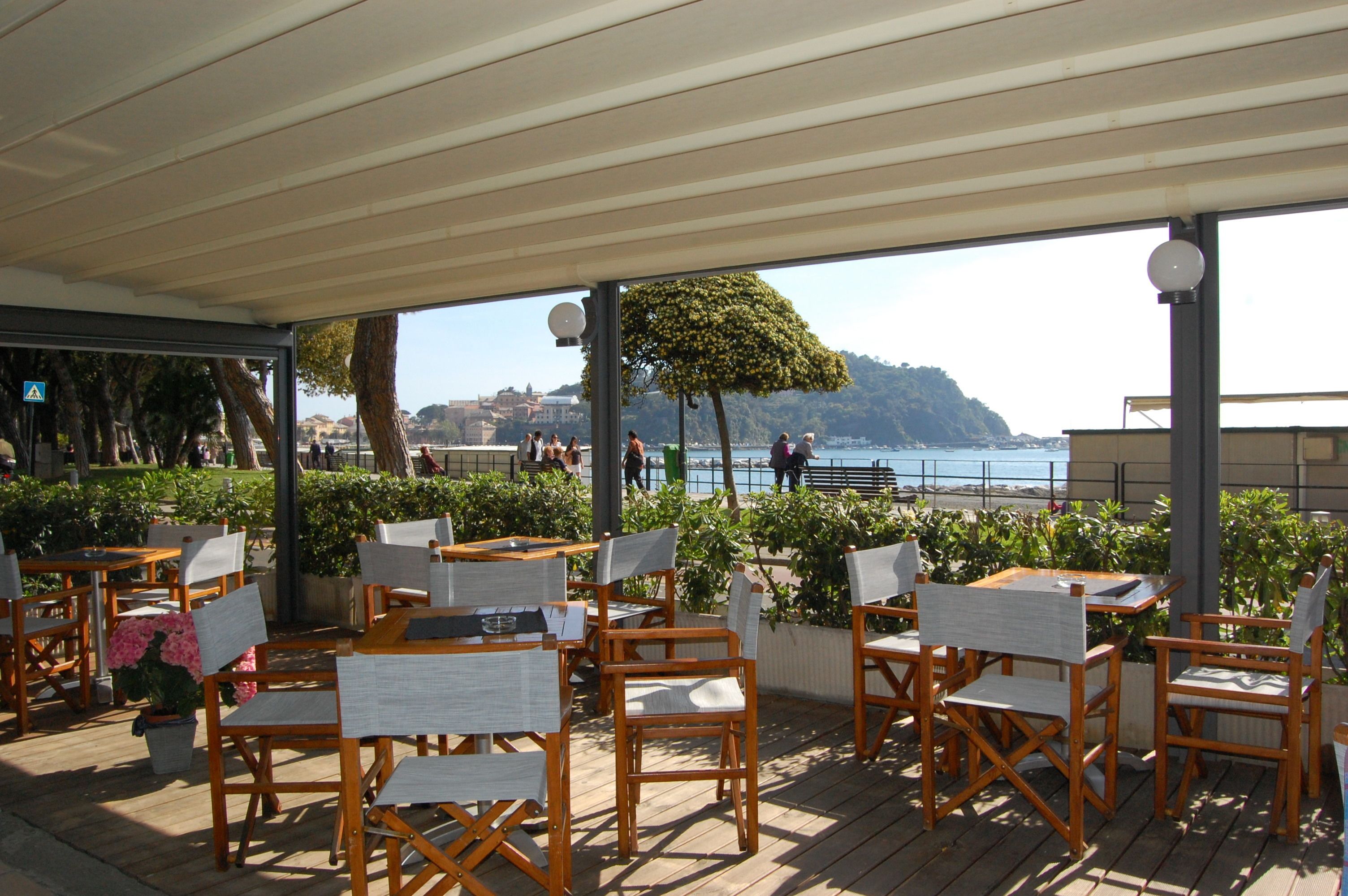 Un espace extérieur aménagé avec des tables et des chaises en bois, une vue sur la mer et une colline en arrière-plan.