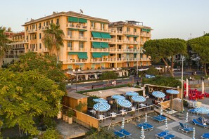 Un hôtel à plusieurs étages doté de balcons, d’un espace extérieur avec des tables et des parasols, et offrant une vue sur la rue.