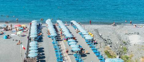 Una playa con hileras de sombrillas azules y blancas, un bar y una estructura de madera.