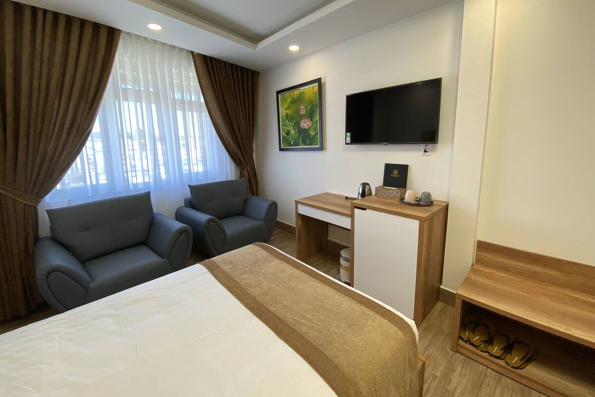 A hotel room with a bed, two sofas, a desk, a TV, and a shoe rack.