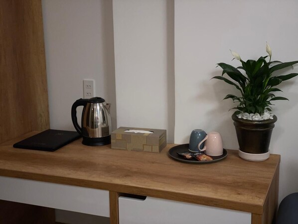 Un bureau en bois avec une bouilloire, une boîte de mouchoirs, une tasse, une assiette avec des collations et une plante en pot.
