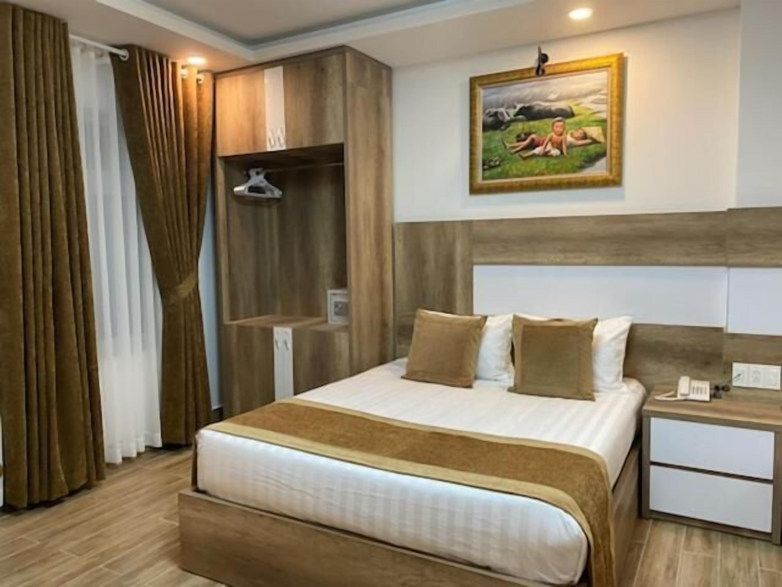 A hotel room with a bed, a nightstand, a painting on the wall, and a wardrobe with a mirror.