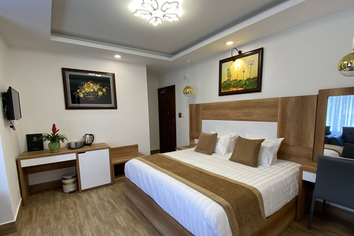 A hotel room with a bed, a desk, a chair, a TV, and a painting on the wall.