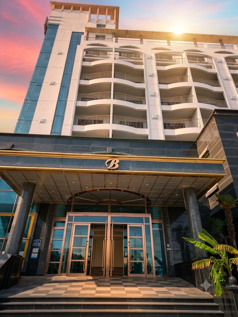 Hotel de vários andares com entrada imponente, piso xadrez e uma grande planta em vaso à direita.