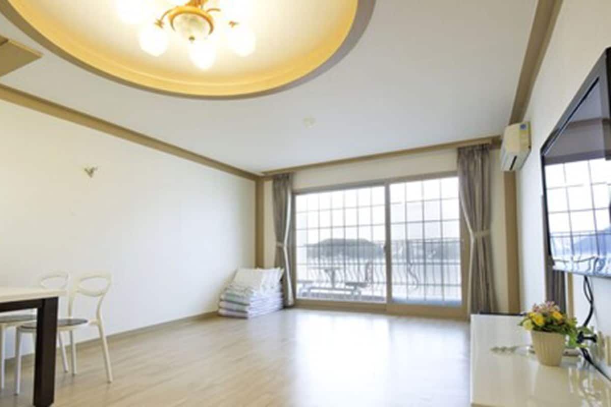 Una habitación amplia con zona de comedor, ventanas grandes y una lámpara de techo.