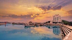 A waterfront scene with a building, boats, and a calm body of water reflecting the sky.