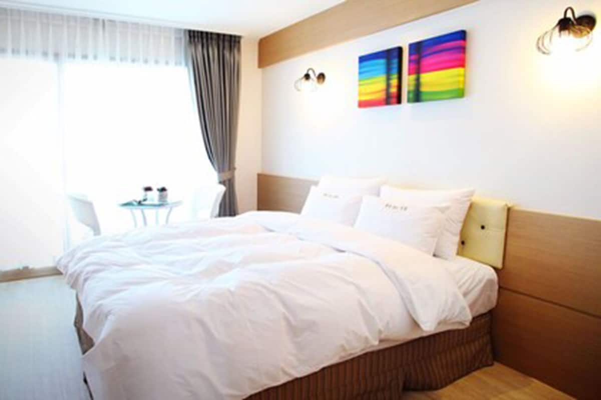 Una habitación de hotel con una cama grande, una mesita con dos sillas y un ventanal con cortinas.