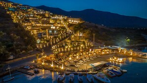 A coastal resort with multiple buildings, a marina with boats, and a well-lit beachfront area. - Royal Marmin Bay Boutique & Art Hotel - Adults Only (Agios Nikolaos)