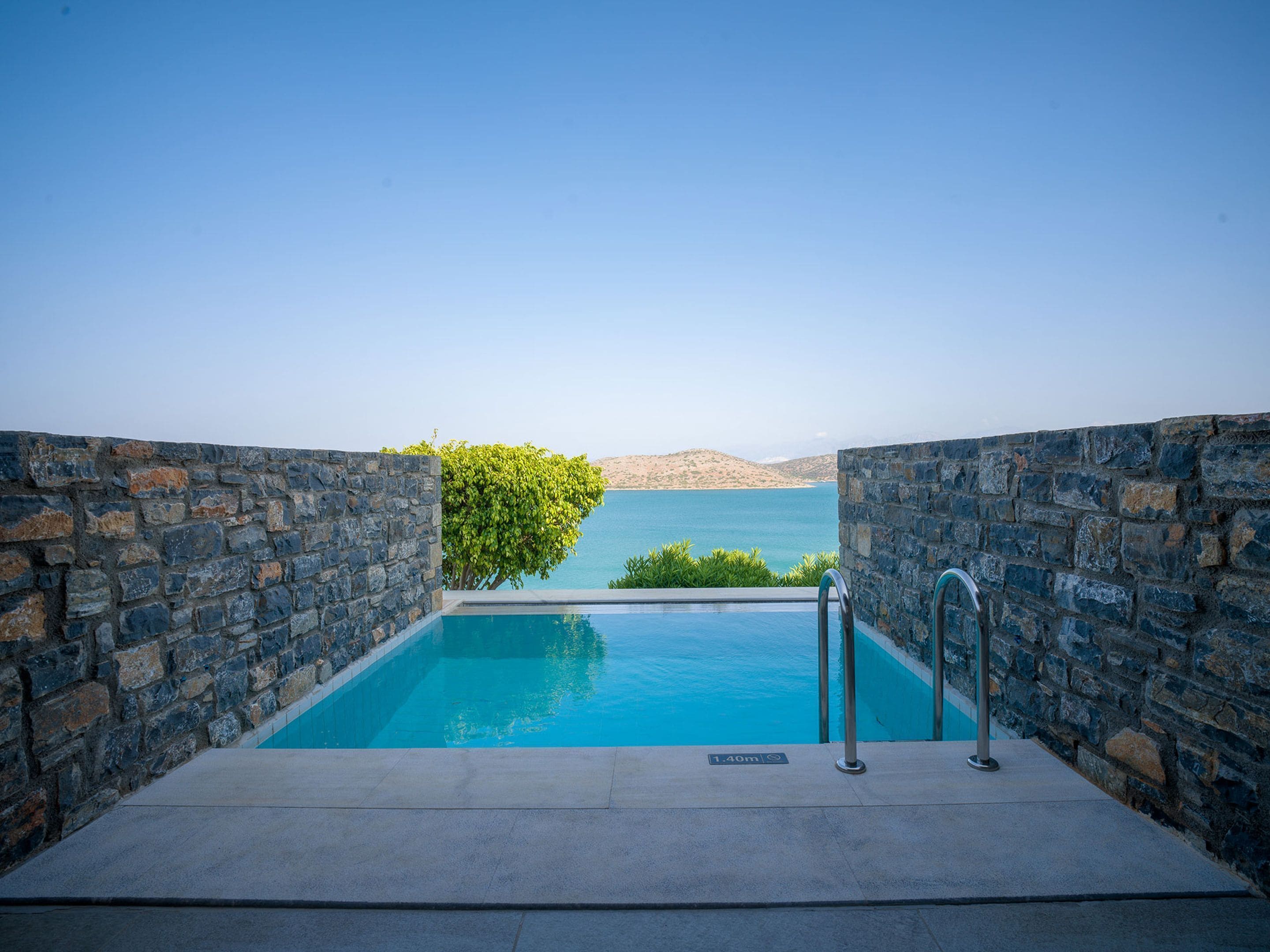 Una piscina infinita de paredes de piedra con vistas despejadas al mar y las colinas.