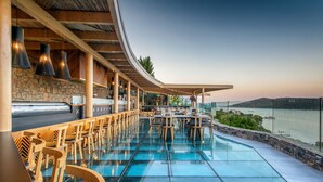A restaurant with a glass floor overlooking a body of water, wooden chairs, and a stone wall. - Royal Marmin Bay Boutique & Art Hotel - Adults Only (Agios Nikolaos)