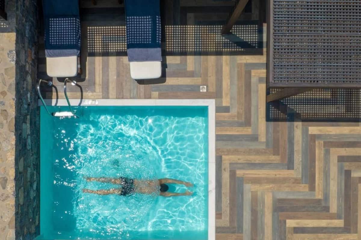 Une piscine où une personne nage, des chaises longues et un sol à motifs.