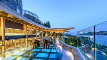 A rooftop bar with glass flooring, outdoor seating, and a view of the sea.