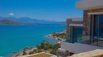 A modern building with a stone facade overlooking a coastal area with clear blue waters and distant mountains.