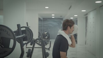 A gym with weightlifting equipment and a person using a white towel.
