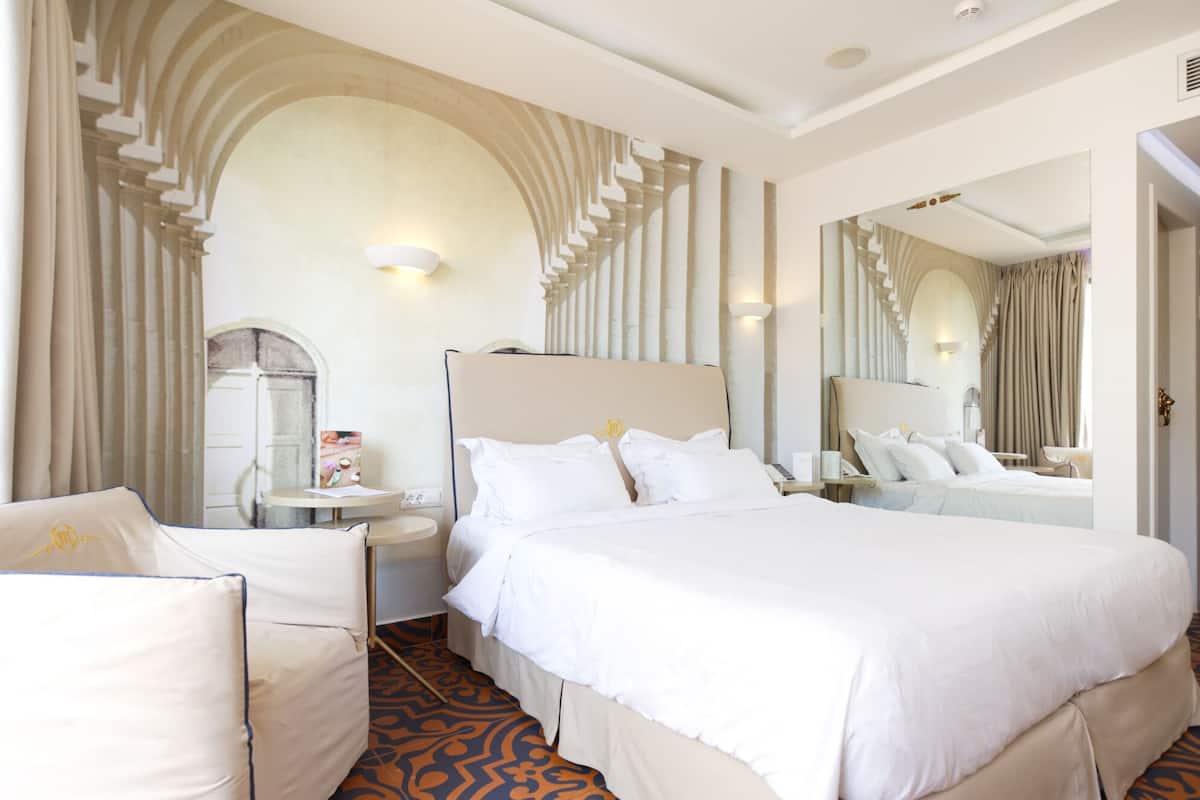 Une chambre d’hôtel avec un grand lit, une table de chevet, une chaise et un miroir.